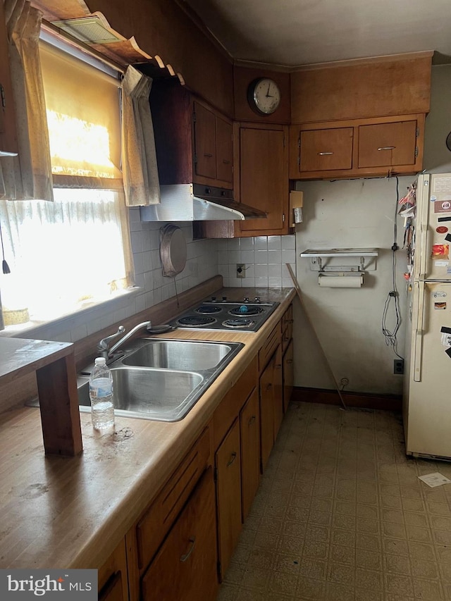 kitchen with a sink, under cabinet range hood, freestanding refrigerator, electric stovetop, and brown cabinets