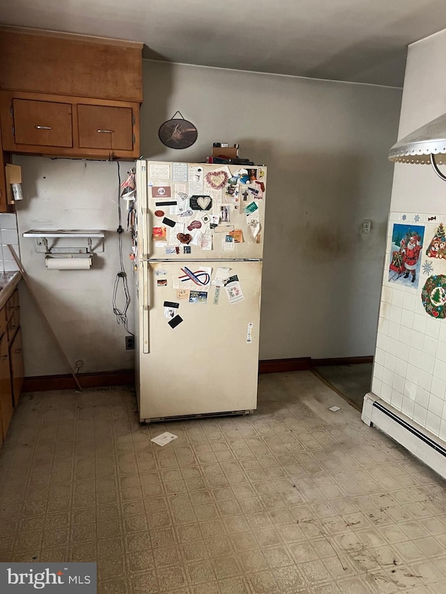 kitchen featuring freestanding refrigerator, brown cabinetry, a baseboard heating unit, and baseboards