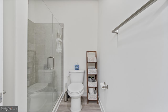 bathroom with toilet, wood finished floors, and a stall shower