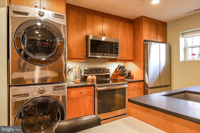 1702 Seaton St NW, Washington, DC 20009 - kitchen with appliances with stainless steel finishes, stacked washing machine and dryer, dark countertops, brown cabinetry, and backsplash