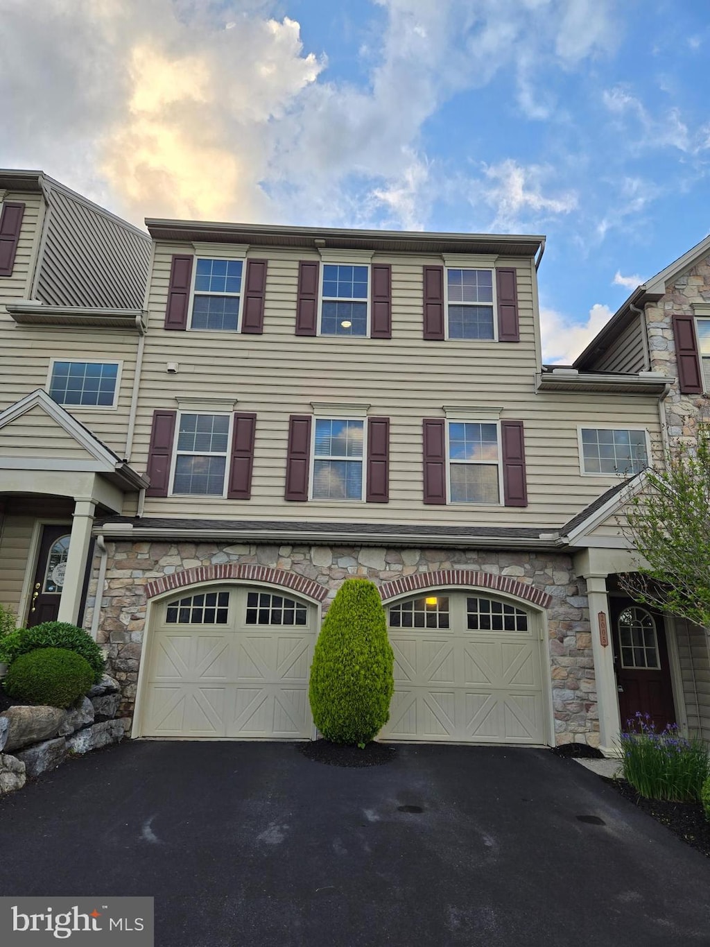 multi unit property with driveway, a garage, and stone siding