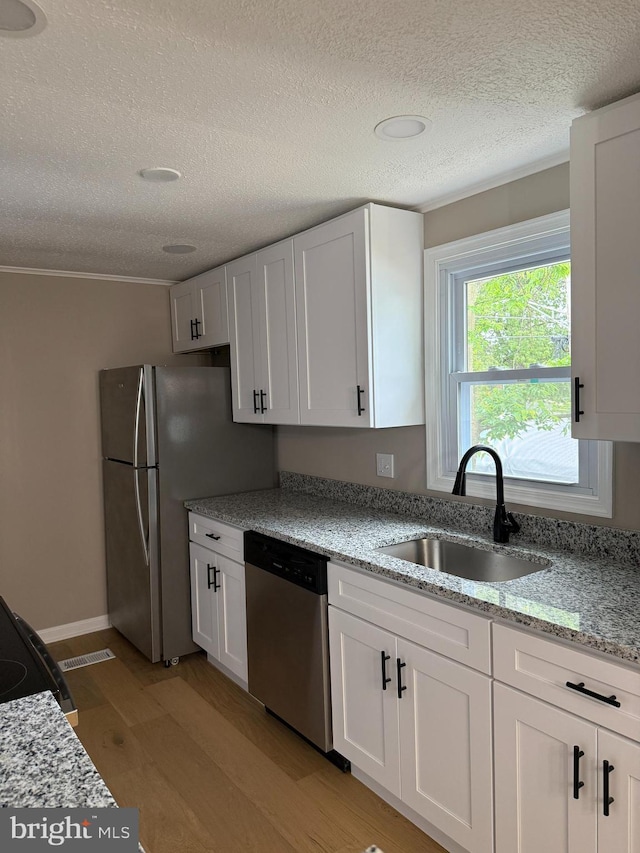 7106 E Spring St, Landover, MD 20785 - kitchen with appliances with stainless steel finishes, a sink, a textured ceiling, light wood-style floors, and white cabinets