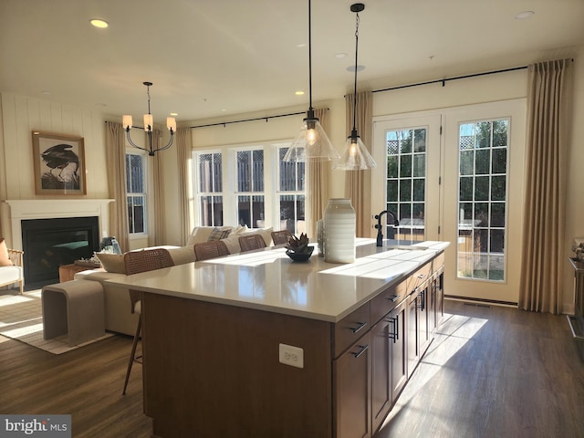 kitchen featuring dark wood finished floors, light countertops, open floor plan, a kitchen island with sink, and a glass covered fireplace