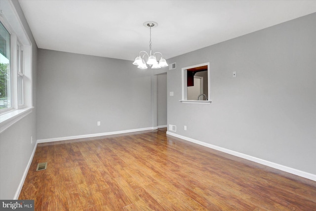 spare room with a chandelier, baseboards, and wood finished floors