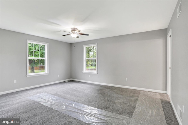 empty room with carpet floors, a ceiling fan, plenty of natural light, and baseboards