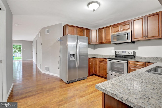 kitchen with stainless steel appliances, light wood-style flooring, brown cabinetry, and light stone counters
