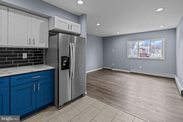 kitchen with stainless steel fridge with ice dispenser, baseboard heating, light wood-style flooring, blue cabinetry, and backsplash