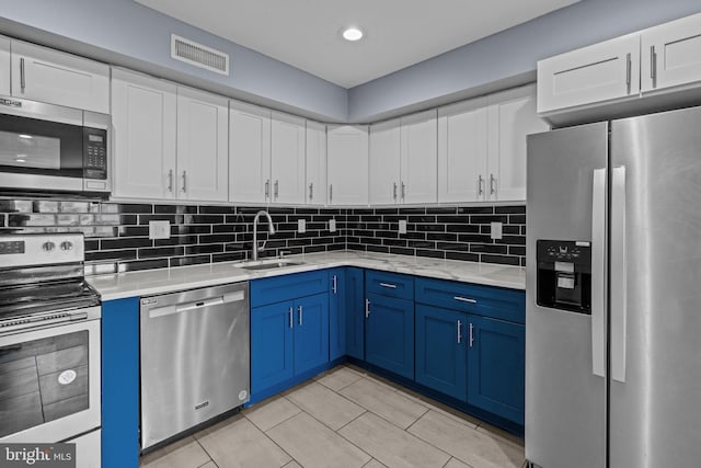 kitchen with appliances with stainless steel finishes, a sink, blue cabinetry, white cabinetry, and recessed lighting