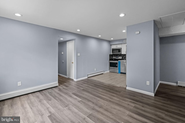 unfurnished living room featuring a baseboard heating unit, attic access, wood finished floors, recessed lighting, and baseboards