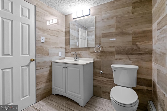 bathroom with tile walls, baseboard heating, a textured ceiling, toilet, and vanity
