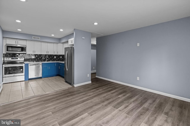 kitchen featuring stainless steel appliances, a sink, light wood-style flooring, white cabinets, and recessed lighting