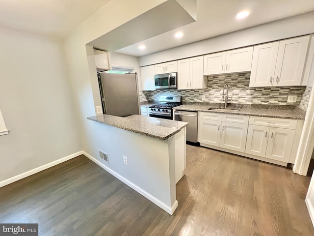 kitchen with appliances with stainless steel finishes, a sink, white cabinetry, wood finished floors, and tasteful backsplash
