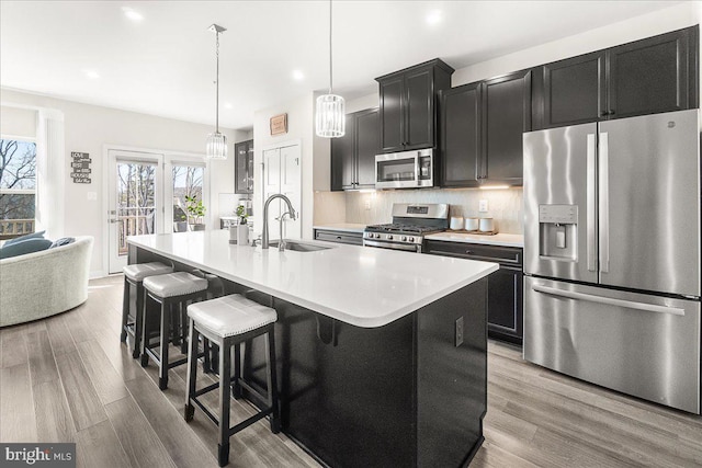 6034 Goshawk St, New Market, MD 21774 - kitchen featuring appliances with stainless steel finishes, a sink, dark cabinetry, a center island with sink, and a kitchen bar