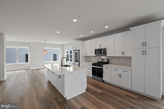 kitchen with appliances with stainless steel finishes, a sink, dark wood-type flooring, a kitchen island with sink, and recessed lighting