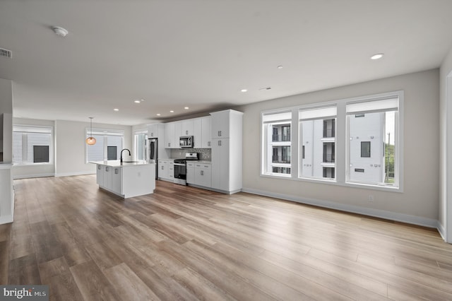 unfurnished living room featuring a sink, baseboards, light wood-style flooring, and recessed lighting