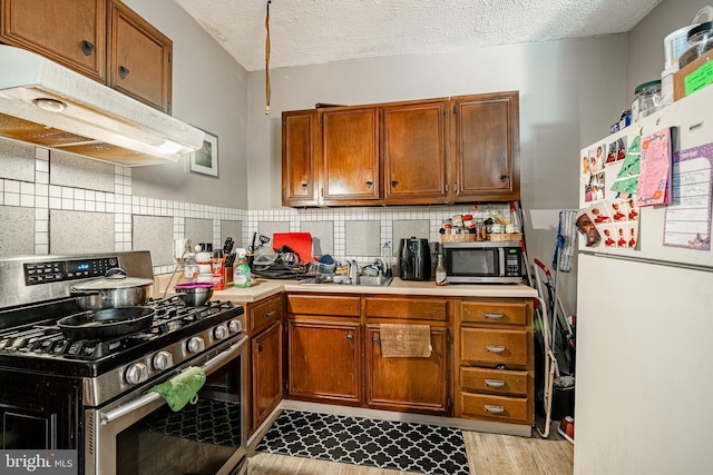 722 E 22nd St, Wilmington, DE 19802 - kitchen featuring appliances with stainless steel finishes, under cabinet range hood, light countertops, brown cabinetry, and a textured ceiling