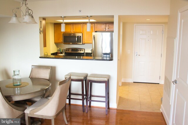 kitchen featuring appliances with stainless steel finishes, dark countertops, decorative light fixtures, tile patterned flooring, and a breakfast bar area