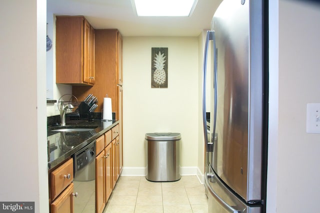 kitchen featuring appliances with stainless steel finishes, a sink, light tile patterned floors, and brown cabinets