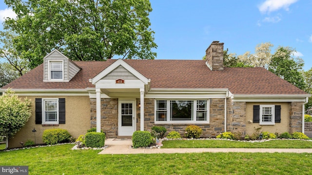 view of front of property with stone siding, a front lawn, a chimney, and roof with shingles