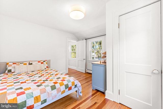 bedroom with lofted ceiling, light wood-style floors, baseboard heating, and baseboards