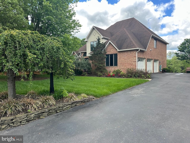 view of front of house featuring a garage, brick siding, asphalt driveway, and a front yard
