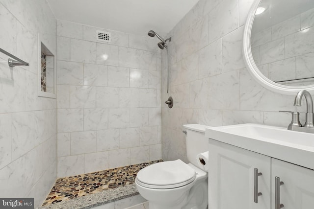 full bathroom featuring tile walls, tiled shower, vanity, and toilet