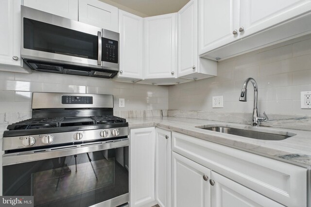 kitchen featuring appliances with stainless steel finishes, white cabinets, a sink, and decorative backsplash