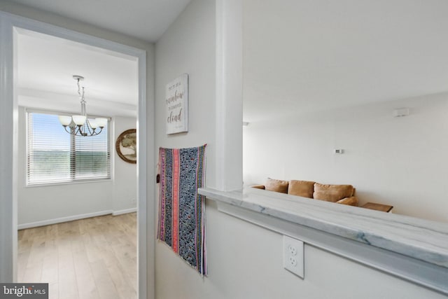 hallway featuring a chandelier, light wood finished floors, and baseboards