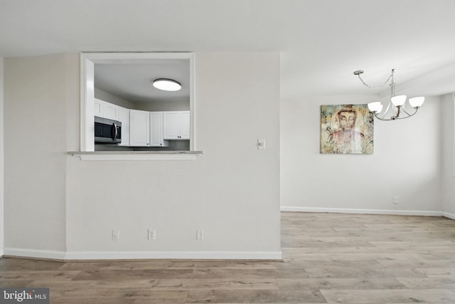 unfurnished dining area with light wood finished floors, a chandelier, and baseboards