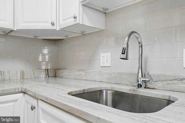 kitchen featuring a sink, backsplash, white cabinets, and light stone counters