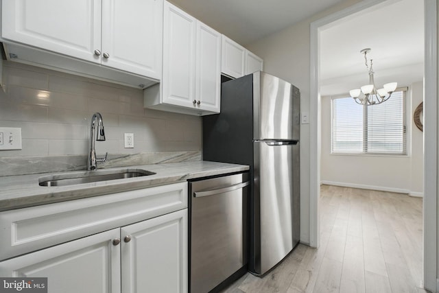 kitchen with stainless steel appliances, a sink, white cabinets, tasteful backsplash, and a chandelier