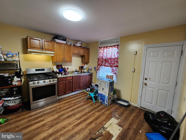 kitchen with stainless steel gas stove, under cabinet range hood, dark wood finished floors, light countertops, and a sink