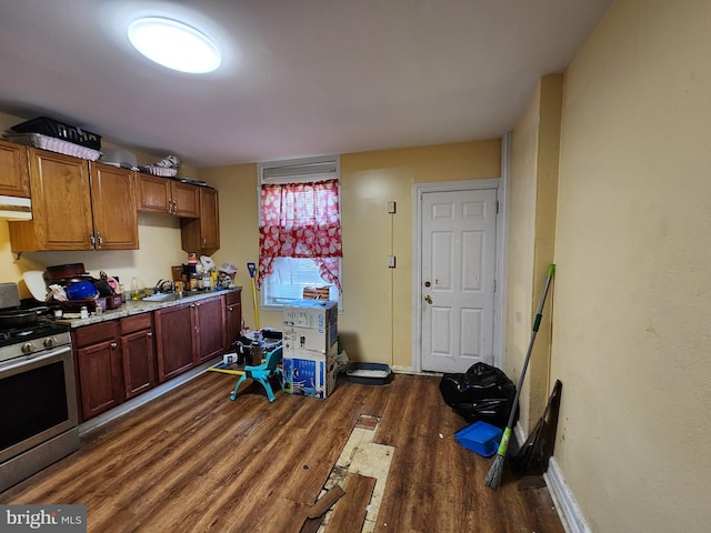kitchen featuring stainless steel gas stove, dark wood-style floors, a sink, under cabinet range hood, and baseboards