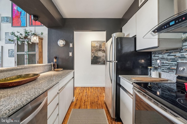 kitchen with appliances with stainless steel finishes, white cabinetry, light wood-style floors, backsplash, and under cabinet range hood