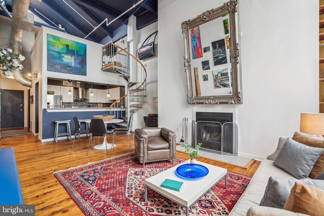 living room featuring stairs, wood finished floors, a fireplace with flush hearth, a high ceiling, and baseboards