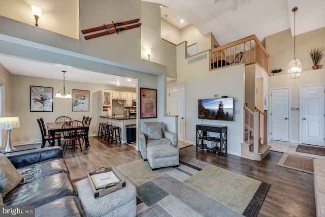 living room with a chandelier, wood finished floors, stairway, high vaulted ceiling, and baseboards