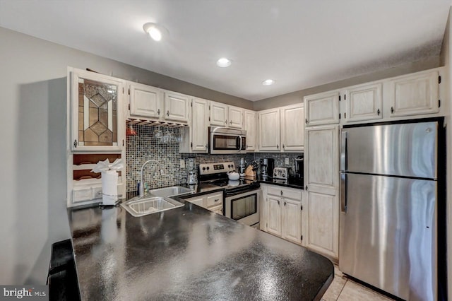 kitchen featuring stainless steel appliances, a sink, dark countertops, backsplash, and a peninsula