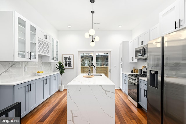 kitchen with appliances with stainless steel finishes, a sink, light stone countertops, decorative backsplash, and dark wood finished floors
