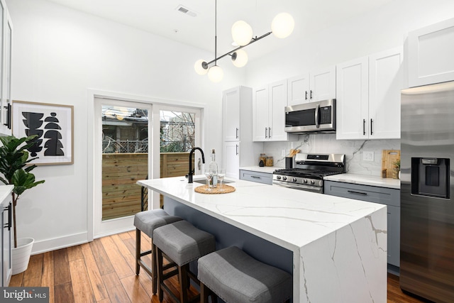 kitchen featuring stainless steel appliances, a sink, light stone countertops, decorative backsplash, and light wood finished floors
