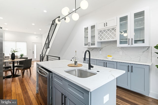 kitchen with a sink, a kitchen island with sink, dark wood-style floors, light stone countertops, and tasteful backsplash