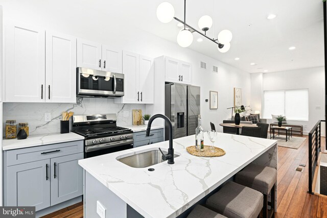 kitchen featuring appliances with stainless steel finishes, a sink, tasteful backsplash, wood finished floors, and recessed lighting