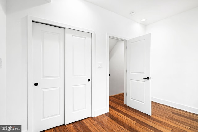 unfurnished bedroom with a closet, dark wood-style flooring, and baseboards