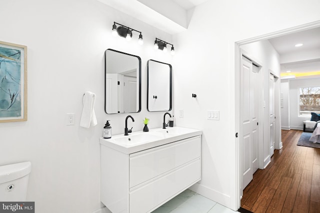 bathroom featuring baseboards, double vanity, toilet, and recessed lighting
