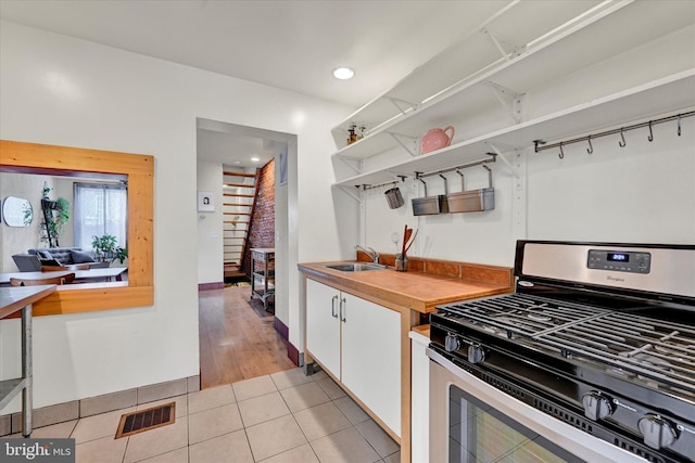 kitchen featuring stainless steel gas range, open shelves, a sink, light tile patterned floors, and white cabinetry