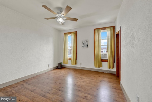 unfurnished room featuring a textured wall, wood finished floors, a ceiling fan, and baseboards