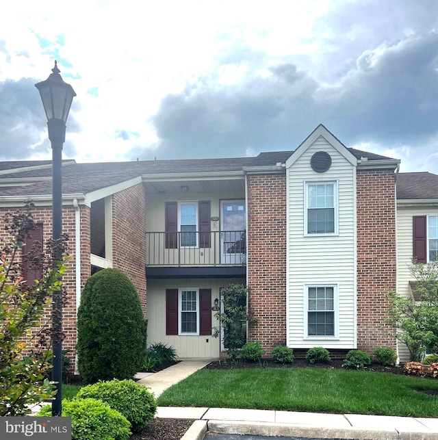 multi unit property with brick siding, a front yard, and a balcony
