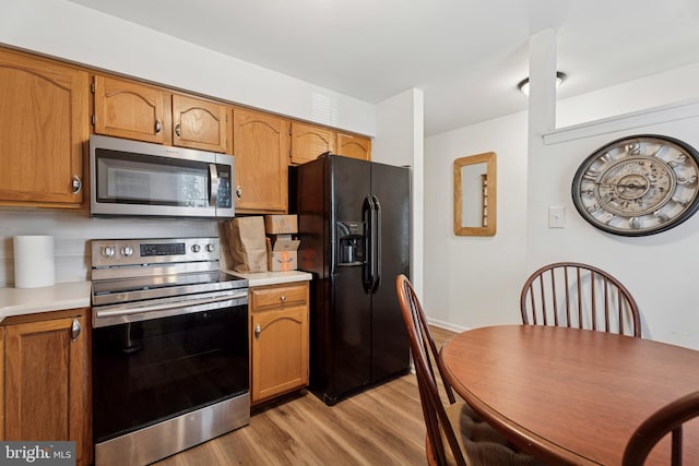 kitchen with appliances with stainless steel finishes, light wood-style flooring, light countertops, and brown cabinetry