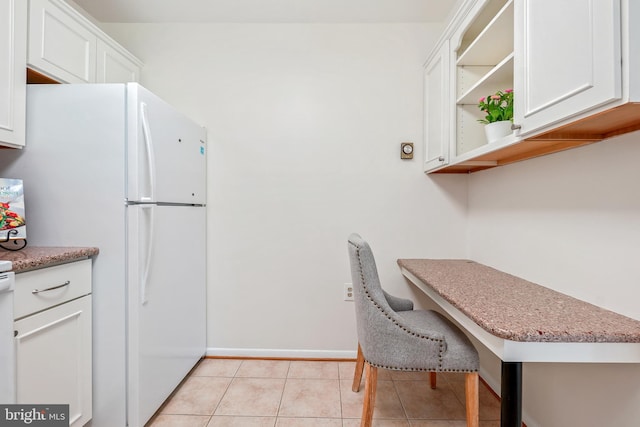 kitchen featuring freestanding refrigerator, baseboards, white cabinetry, light tile patterned flooring, and light stone countertops