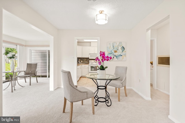dining area with light carpet, baseboards, and a textured ceiling