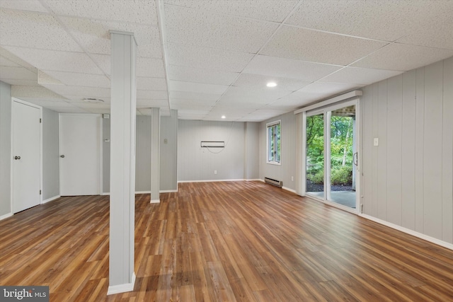 below grade area featuring wood finished floors, baseboard heating, a drop ceiling, and baseboards